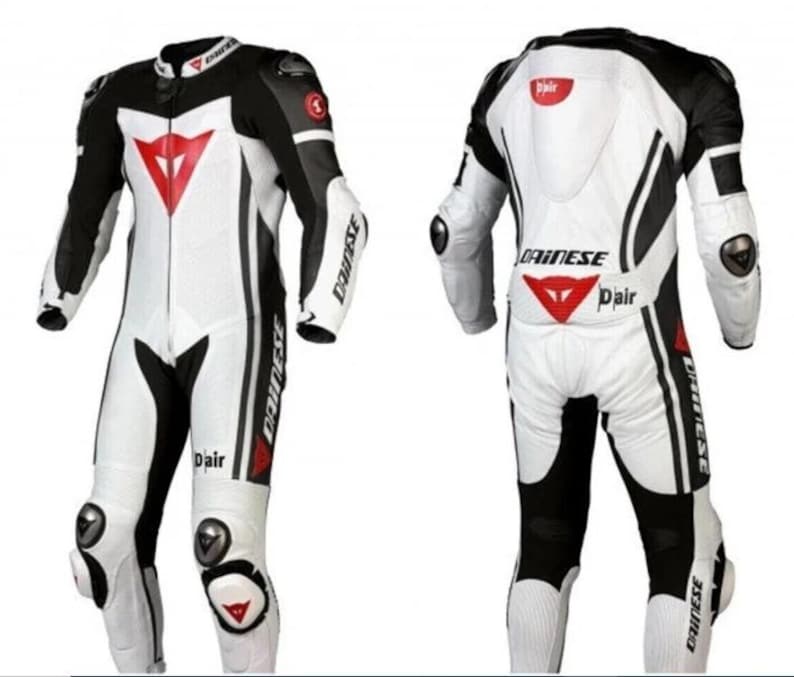 Puede incluir: Traje de carreras de moto blanco y negro con detalles en rojo. El traje presenta un logotipo triangular rojo en el pecho y la espalda, con la marca "Dainese" visible. Incluye protectores de rodillas y codos.
