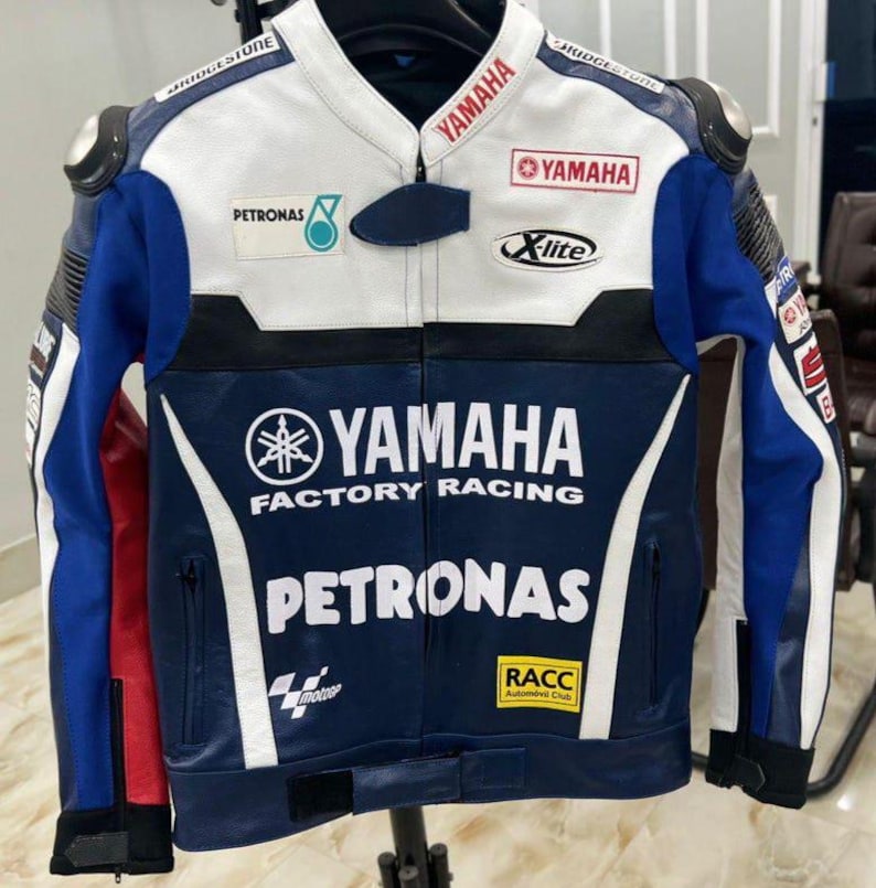 Puede incluir: Una chaqueta de carreras de motos azul, blanca y roja con logotipos de Yamaha Factory Racing, Petronas, Bridgestone, X-lite y RACC. La chaqueta cuenta con cierre de cremallera frontal, cuello con broche y varios logotipos de patrocinadores impresos.