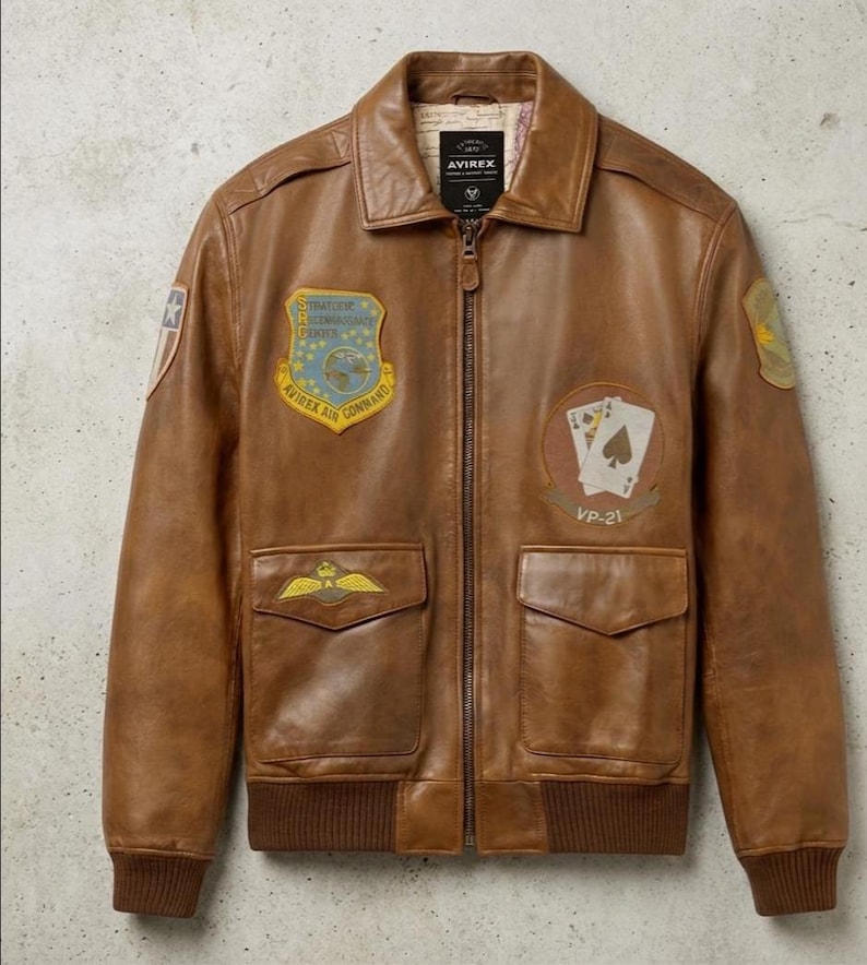 May include: Brown leather bomber jacket with multiple patches and pockets. The jacket features a zip-up front, a ribbed hem and cuffs, and a classic collar. Patches include the text "Strategic Reconnaissance Center" and a playing card design.