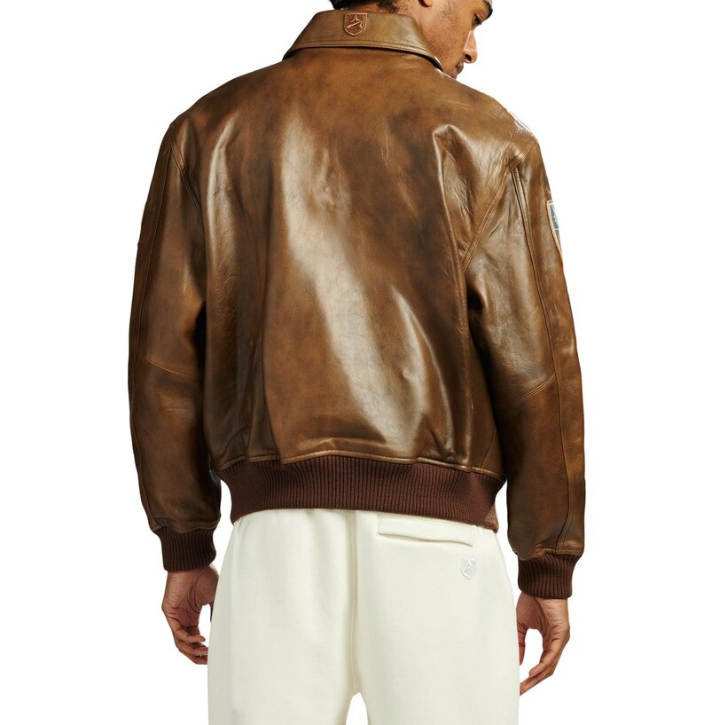 May include: A brown leather bomber jacket with a classic collar and ribbed cuffs and hem. The jacket has a distressed finish, giving it a vintage look. The jacket is a medium weight and appears to be well-constructed.