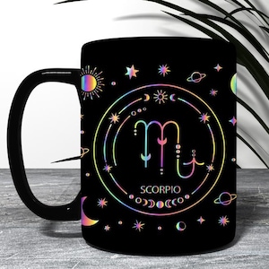 May include: A black ceramic mug featuring a holographic Scorpio zodiac symbol centered within a circular frame. The design includes celestial motifs like stars, moons, planets, and suns in a rainbow metallic finish, with the word SCORPIO printed below.