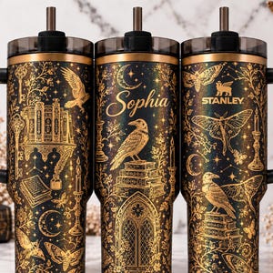 May include: Three black Stanley tumblers with gold-toned illustrations of ravens, moths, books, keys, and candles. The center tumbler features the name Sophia in script. Each tumbler has a black handle, a dark lid, and a straw.