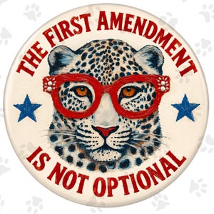 May include: A circular button featuring a leopard wearing red glasses. The text THE FIRST AMENDMENT IS NOT OPTIONAL is printed in red around the leopard. Two blue stars are positioned on the left and right sides of the leopard's face.