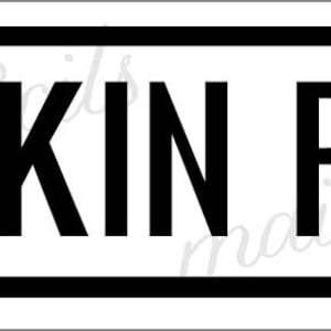 May include: A rectangular sign with a white background and a thick black border. The text PUMPKIN PATCH is printed in large, bold, black sans-serif capital letters centered within the frame. The sign features small semi-circular tabs on both sides.