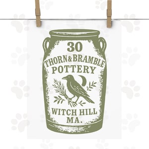 May include: A green and white print featuring a stylized jar with the text "30 Thorn & Bramble Pottery" and "Witch Hill MA." A crow holds a sprig of leaves and a crescent moon. The print is held by two wooden clothespins.