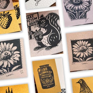 May include: A collection of handmade art cards with various linocut designs. The cards feature images of a squirrel holding an acorn and a sign that reads "MAKE SCISM AGAIN", flowers, strawberries, and pottery. The cards are in shades of black, white, and yellow.