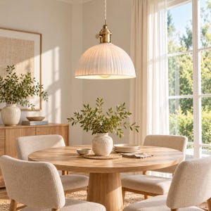 May include: A white ribbed dome pendant light with a brass-toned metal fixture suspended from a cord. The shade features a textured, pleated surface that diffuses light downward, creating a focused illumination over the circular wooden dining table.