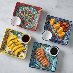 Puede incluir: Cuatro platos cuadrados de cerámica para aperitivos con cuencos para salsa adjuntos. Cada plato presenta un diseño floral colorido e intrincado en rojo, azul, amarillo y verde azulado. Los platos contienen alimentos como empanadillas, camarones, naranjas y tomates.
