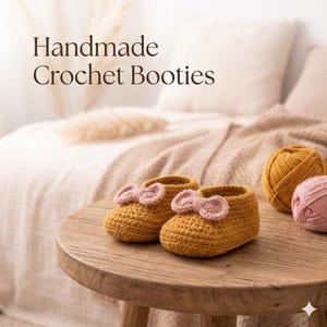 Puede incluir: Un par de patucos de ganchillo color mostaza con un pequeño lazo de ganchillo rosa claro en la parte delantera de cada zapato. El texto Handmade Crochet Booties es visible en la esquina superior izquierda. Dos ovillos de lana, uno mostaza y otro rosa.