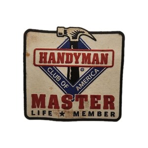 Puede incluir: Un parche bordado cuadrado con fondo blanco roto y borde negro. Presenta un icono de martillo negro sobre un diamante azul que contiene el texto HANDYMAN CLUB OF AMERICA. Debajo, la palabra MASTER está en rojo, con LIFE MEMBER en negro.