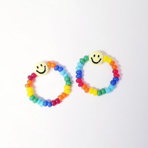 May include: Two rainbow beaded bracelets with a yellow smiley face charm. Each bracelet has red, orange, yellow, green, blue, and purple beads.