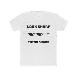 May include: White t-shirt with the text "LOOK SHARP THINK SHARP" in black, above a pixelated sunglasses graphic. The shirt is made of a soft material and has a crew neck.