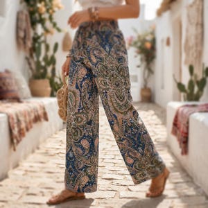 Puede incluir: Pantalones de pernera ancha con estampado de cachemira en tonos azul marino, verde oliva y melocotón. Los pantalones tienen una cintura elástica y una silueta fluida. La tela presenta un patrón detallado y adornado.