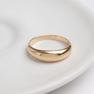 Op de afbeelding: Een gepolijste gouden ring met een glad, afgerond oppervlak en een dik, koepelvormig profiel. De ring heeft een doorlopend, naadloos ontwerp met een hoogglanzende metalen afwerking die het licht reflecteert over de gebogen, gouden buitenkant.