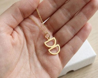 Colar com pingente geométrico minimalista em prata de lei banhada a ouro e estrutura em arco sobreposta.