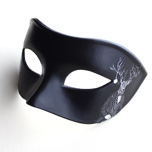 May include: A black masquerade mask with a white design of a deer wearing a suit and bow tie.