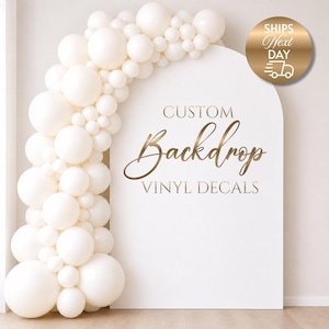 May include: A white backdrop with a curved top, decorated with a cream-coloured balloon arch. The backdrop has gold text reading "CUSTOM Backdrop VINYL DECALS." A gold circle with "SHIPS Next DAY" is in the upper right corner.