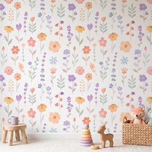 May include: A wall covered in a floral wallpaper pattern featuring watercolor-style flowers in shades of orange, yellow, purple, and pink. A small wooden stool holds a purple mug. A wicker basket contains stuffed animals. A wooden deer and a colorful stacking toy are on the floor.