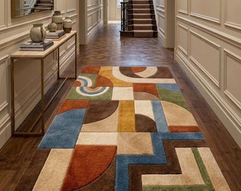 May include: A rectangular area rug featuring a geometric pattern of interlocking shapes in shades of blue, brown, tan, orange, and green. The design consists of circles, semicircles, and straight lines arranged in a structured, multi-colored layout.