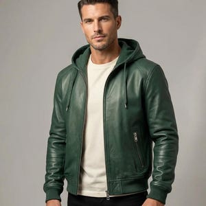 May include: A green leather hooded jacket with a zip-up front and a small chest pocket. The jacket has a ribbed hem and cuffs. The model is wearing a white t-shirt underneath. The jacket is a dark shade of green.