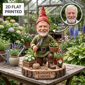 Könnte beinhalten: Eine 2D-flachgedruckte Gartenzwerg-Statue mit personalisiertem Foto. Der Zwerg kniet und hält eine Schaufel und einen Korb mit Pflanzen. Die Basis ist eine Holzscheibe mit dem Text "Grandpa's Garden".