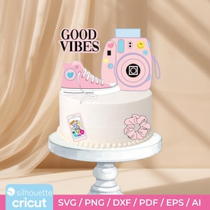 May include: A cake with pink decorations, including a high-top sneaker, a camera, a scrunchie, and a phone with the text "Vacay You". The cake is topped with the words "Good Vibes".