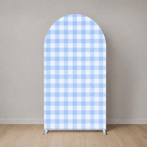 Puede incluir: Un telón de fondo alto y arqueado con un patrón de cuadros vichy azul claro y blanco. El telón de fondo se apoya en dos patas de metal plateado. Está colocado contra una pared gris neutra y un suelo de madera.