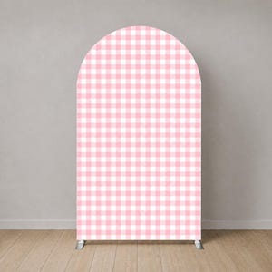 May include: A large, arched backdrop featuring a pink and white gingham design. The backdrop is supported by silver legs and stands against a neutral grey wall and light wood floor. The design is a classic, cheerful pattern.