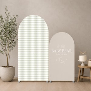 Può includere: Due coperture per fondali ad arco. La copertura più alta presenta un motivo a quadretti beige e bianco. La copertura più piccola è beige tinta unita e mostra il testo bianco A little BABY BEAR IS ON THE WAY con icone di luna e stelle.