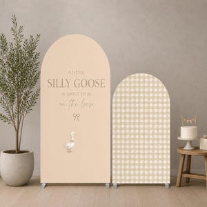 Può includere: Due coperture per fondali ad arco. Quella più alta è beige con il testo A LITTLE SILLY GOOSE IS ABOUT TO BE on the loose, una piccola icona a fiocco e un'illustrazione di un'oca. Quella più corta presenta un motivo a quadri beige e bianco.