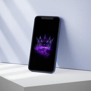 Op de afbeelding: Een smartphone met een zwart scherm met een paars en zwart kroonontwerp. De telefoon heeft een blauwe rand en leunt tegen een wit en blauw oppervlak. Het kroonontwerp heeft scherpe punten en een rokerige paarse achtergrond.