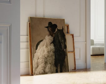 May include: A framed wall art print featuring a person wearing a wide-brimmed black hat and a voluminous, layered cream-colored ruffled gown standing beside a dark-coated horse. The artwork is set against a muted, neutral-toned background.