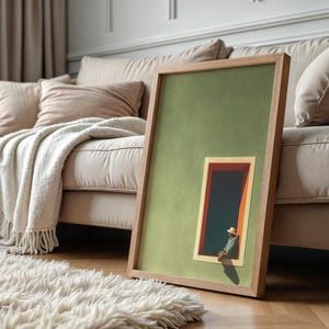 May include: A framed rectangular wall art piece featuring a solid sage green background with a smaller inset illustration of a person wearing a straw hat sitting in a dark doorway with orange trim, all enclosed in a light-toned wooden frame.