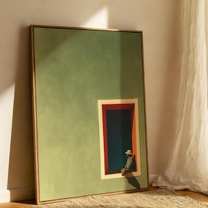 May include: A framed rectangular wall art piece featuring a large sage green field with a smaller inset rectangular window frame. Inside the window, a figure wearing a hat sits against a dark blue background with red and orange trim accents.