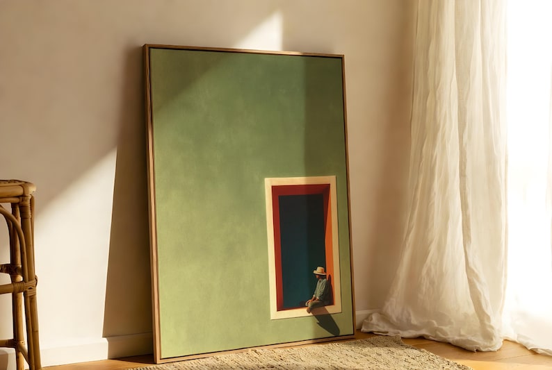 May include: A framed rectangular wall art piece featuring a large sage green field with a smaller inset rectangular window frame. Inside the window, a figure wearing a hat sits against a dark blue background with red and orange trim accents.