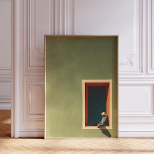 May include: A framed rectangular wall art print featuring a solid olive green wall with a single rectangular window frame in orange and cream. A small figure wearing a straw hat sits on the window ledge, casting a long shadow on the green wall.