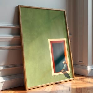 May include: A framed rectangular wall art piece featuring a solid olive green background with a smaller inset rectangular window. The window has a red and cream border and contains a dark blue interior with a small figure wearing a hat sitting inside.