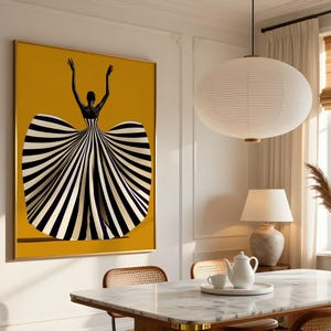May include: A rectangular wall art print featuring a figure with arms raised, wearing a voluminous gown with bold black and white vertical stripes against a solid mustard yellow background, framed in a thin gold border on a white wall.