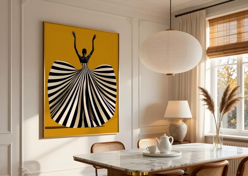May include: A rectangular wall art print featuring a figure with arms raised, wearing a voluminous gown with bold black and white vertical stripes against a solid mustard yellow background, framed in a thin gold border on a white wall.