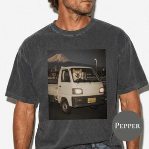 Könnte beinhalten: Ein anthrazitfarbenes Kurzarm-T-Shirt mit einem Grafikdruck eines weißen Kei-Trucks, in dessen Fahrersitz ein Shiba Inu sitzt. Der Truck hat ein gelbes Nummernschild mit der Aufschrift 48-315 und einen Berg im Hintergrund, der dem Fuji ähnelt.