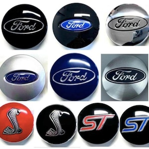 May include: A collection of Ford car wheel center caps in various colors, including black, silver, and blue. Some caps feature the Ford logo in silver, while others have a blue oval. Additional caps display a cobra emblem and ST lettering.