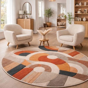 May include: A round area rug with a geometric design in shades of orange, brown, gray, and cream. Two cream-colored armchairs sit on either side of the rug. The room has a neutral color palette with wooden furniture and natural light.