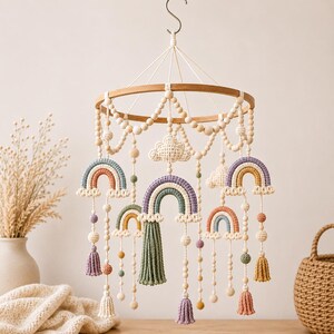 May include: A handcrafted baby mobile featuring multiple crochet rainbows in various colors, including blue, orange, and purple. The mobile is suspended from a wooden ring with wooden beads and tassels, creating a whimsical nursery decoration.