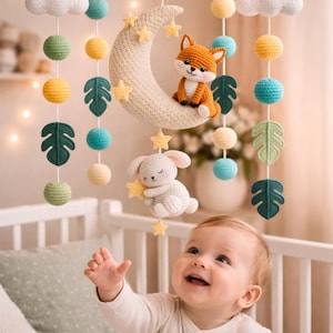 Könnte beinhalten: Handgefertigtes Baby-Mobile mit Mond, Sternen, Fuchs und Häschen. Das Mobile enthält weiße Wolken, grüne, gelbe und türkisfarbene Kugeln sowie grüne Blattformen. Das Mobile hängt über einem Babybett.