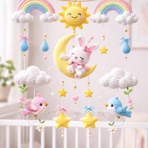 May include: A handmade crochet baby mobile featuring a smiling yellow sun, rainbows, clouds, stars, and a bunny on a crescent moon. The mobile includes pink and blue birds, and teardrop accents, all in soft pastel colors.