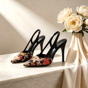 Puede incluir: Un par de zapatos de tacón negros con estampado floral. Los zapatos tienen punta afilada y tiras finas. Los tacones miden aproximadamente 10 cm de alto. El diseño floral incluye flores rojas, naranjas y amarillas sobre un fondo oscuro.