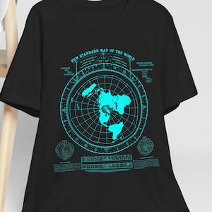Könnte beinhalten: Schwarzes T-Shirt mit einer türkisfarbenen Weltkarten-Grafik und dem Text "NEW STANDARD MAP OF THE WORLD". Das Kartendesign enthält Rasterlinien und Textdetails. Eine weiße Baseballkappe hängt an einem Holzstuhl.