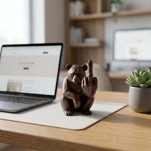 May include: A dark brown bear figurine sitting in an upright position with its right arm raised and its middle finger extended in a gesture. The bear has detailed fur texture, pointed ears, and a focused facial expression, crafted as a desk ornament.