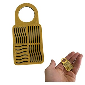 May include: A gold-colored door hanger with a circular opening at the top and a rectangular body. The body features a pattern of vertical and wavy black lines. A smaller version of the door hanger is held in a hand.