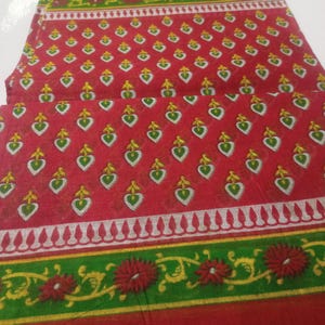 Könnte beinhalten: Roter Stoff mit einem sich wiederholenden Muster aus grünen und weißen Herzen mit gelben Akzenten. Der Stoff hat einen grün-gelben Blumenrand mit roten Blumen und einen weißen Zierrand.